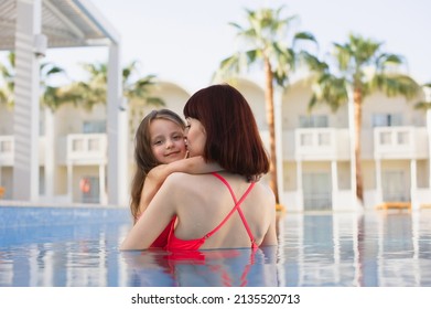 Happy Caucasian Mother And Her Little Cute Daughter Playing In Swimming Pool. Mother And Baby Girl Swim In The Pool. Mom Holding Her Daughter In Her Arms In The Pool And Teaching Her To Swim