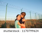 happy caucasian mother refugee reunited with child kissing her near fence barbed wire