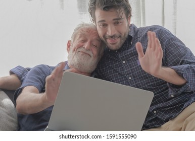 Happy Caucasian Old Father And Son Family Making Video Conference Via Laptop Computer With Smiling Faces In Cozy Living Room House. Technology Connecting People Concept, Selective Focus.