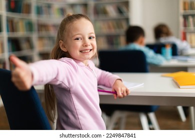 Happy caucasian schoolgirl gesturing thumbs up and smiling to camera, sitting at school in classroom with multiracial kids, free space. Education concept - Powered by Shutterstock