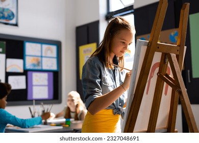 Happy caucasian schoolgirl painting using brush and easel in school art class. School, education, creativity and learning concept. - Powered by Shutterstock