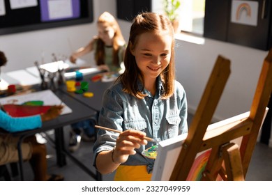 Happy caucasian schoolgirl painting using brush and easel in school art class. School, education, creativity and learning concept. - Powered by Shutterstock