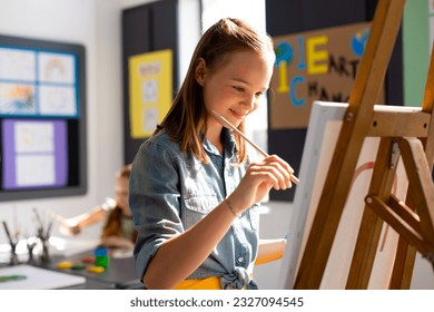 Happy caucasian schoolgirl painting using brush and easel in school art class. School, education, creativity and learning concept. - Powered by Shutterstock