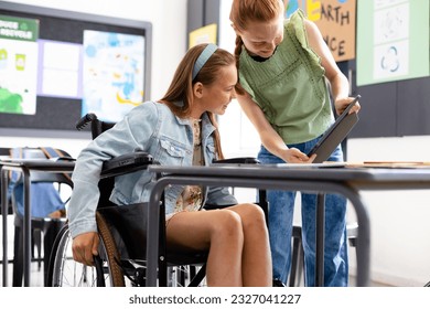 Happy caucasian schoolgirl in wheelchair with her friend using tablet in school classroom. Education, inclusivity, school, learning and disability concept. - Powered by Shutterstock