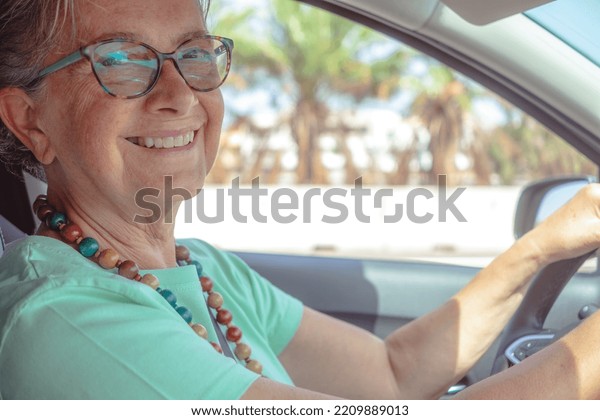 Happy caucasian senior woman driving the car\
smiling looking at camera