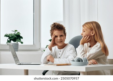 Happy Caucasian siblings typing on laptops while studying online at home, surrounded by books and educational materials They are sitting at a table in their comfortable living room, concentrating on - Powered by Shutterstock