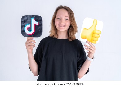 Happy Caucasian Teen Girl In Black T-shirt Holding Tiktok Logo And Thumbs Up Emoji Sign, Isolated On White. Turkey, Istanbul, May 29, 2022.