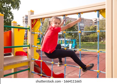 Happy caucasian teenage girl wearing a red T-shirt, having fun on playground, climbing the rope net in summer - Powered by Shutterstock