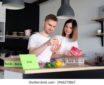 Happy Caucasian White Couple Unpack Online Home Food Delivery. Box With Packed Tuna, Shrimp, Vegetables And Recipe Card On A Kitchen Background. Food Delivery Services. Dinner Set From Restaurant.