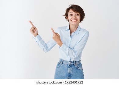 Happy Caucasian Woman In Blue Collar Shirt And Jeans, Smiling Cheerful And Pointing At Upper Left Corner Logo, Standing On White Background.