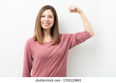Happy Caucasian woman dressed casual and flexing her arm showing her strength and smiling