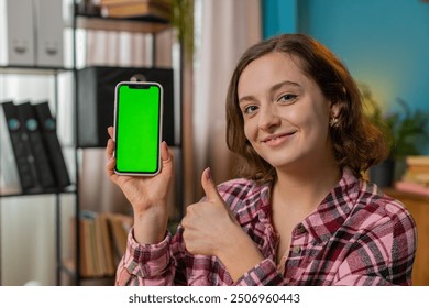 Happy Caucasian woman freelancer looking at camera and showing smartphone with green screen for new application. Business lady gesture thumbs up holding cellphone with chroma key mock up green screen - Powered by Shutterstock