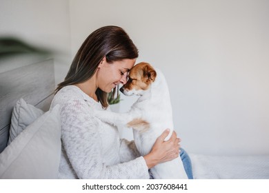 happy caucasian woman at home cuddling on bed with cute jack russell dog. Foreheads together. Pets, love and relax at home