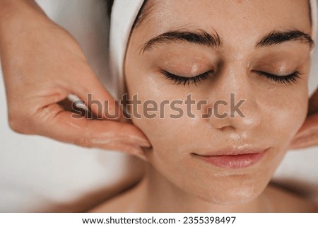 Happy caucasian woman receiving soothing mask or moisturizing cream balm, massaging face at spa salon. Daily spa morning routine.