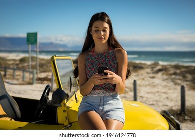 Happy caucasian woman sitting on beach buggy by the sea using smartphone. beach break on summer holiday road trip. - Powered by Shutterstock