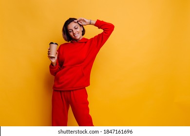 Happy caucasian woman wearing warm winter clothes, hoodie and pants, warm herself with cup of hot coffee, studio shot.