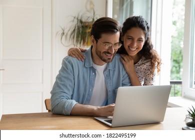 Happy Caucasian young couple look at laptop screen browse surf wireless internet on gadget. Smiling millennial man and woman shopping paying on internet on computer at home. Technology concept. - Powered by Shutterstock