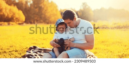 Happy caucasian young father and son child with camera together sitting on the grass in summer sunny evening park