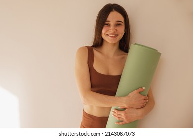 Happy caucasian young girl holding yoga mat smiling at camera on beige background. Pretty woman trainer in sports tight clothes. Healthy lifestyle concept - Powered by Shutterstock
