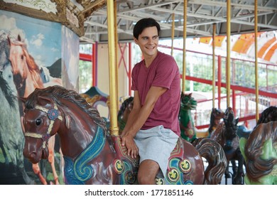 Happy Caucasian Young Handsome Man On Merry Go Round At The Amusement Park