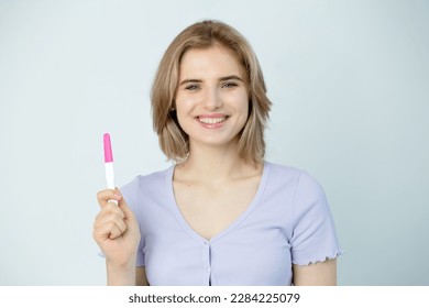 Happy caucasian young woman holding pregnancy test and smilind friendly, close up. Woman looks at pregnancy ovulation test celebrate positive result get pregnan.  IVF concept