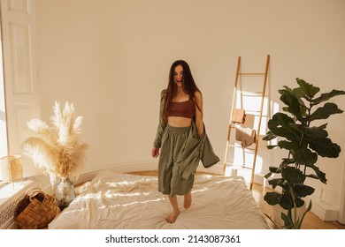 Happy caucasian young woman jumping on mattress in modern living room interior. Brunette girl enjoys freedom and active lifestyle. Leisure concept