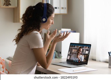 Happy Caucasian Young Woman Look At Laptop Screen Talk Chat On Video Call With African American Man Husband. Smiling Female In Headphones Have Webcam Digital Virtual Communication With Friend.