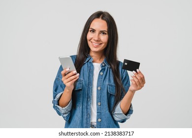 Happy caucasian young woman mobile user bank client customer holding credit card while using mobile e-banking e-commerce application for online shopping, payments, transactions, cashback