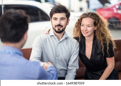 Happy Caucasion couple getting great deal and complete agreement from car rental company officer. Man customer handshake with Asian male staff sitting in office while woman satisfy service with smile.