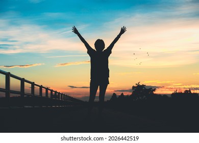 Happy celebrating winning success woman at sunset or sunrise standing elated with arms raised up.