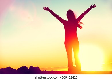 Happy celebrating winning success woman at sunset or sunrise standing elated with arms raised up above her head in celebration of having reached mountain top summit goal during hiking travel trek. - Shutterstock ID 509482420