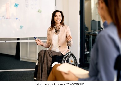 Happy CEO in wheelchair explaining inclusive business strategy to her coworkers during presentation in meeting room.