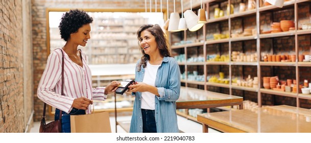 Happy ceramic store owner receiving a contactless credit card payment from a customer in her shop. Successful small business owner smiling cheerfully while serving a customer. - Powered by Shutterstock