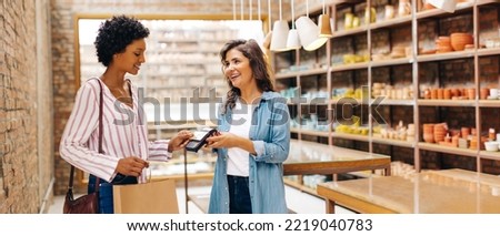 Happy ceramic store owner receiving a contactless credit card payment from a customer in her shop. Successful small business owner smiling cheerfully while serving a customer.