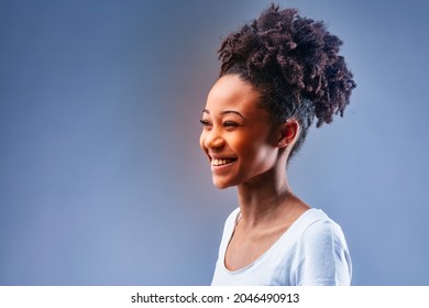 Happy charismatic young Black woman with vivacious smile looking to the side to copyspace over blue in a studio portrait