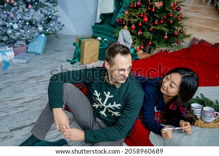 Happy charming asian woman dressed in jersey talking to her handsome boyfriend spending time in a cozy home, romantic couple in love happy about celebrating winter holidays together in good mood.
