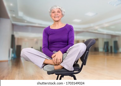 Happy charming beautiful elderly woman is doing exercise on a chair. Exercising gymnastics for health in the fitness room. Sports training.