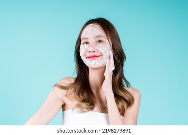 Happy Charming Young Asian Woman Applying Facial Foam Cleanser Wash And Scrub On Her Face On The Blue Background.