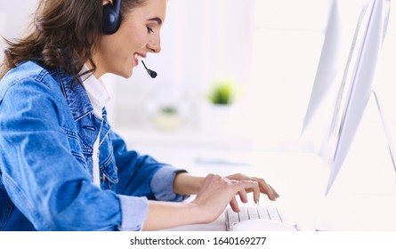 Happy Charming Young Woman Sitting And Working With Laptop Using Headset In Office