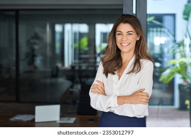 Happy cheerful 45 year old Latin professional mid aged business woman corporate leader, smiling positive mature female executive manager standing in office arms crossed looking at camera, portrait.