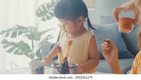 Happy Cheerful Asia Family Mom Teach Toddler Girl Paint Ceramic Pot Having Fun Relax On Table In Living Room At House. Spending Time Together, Social Distance, Quarantine For Coronavirus Prevention.