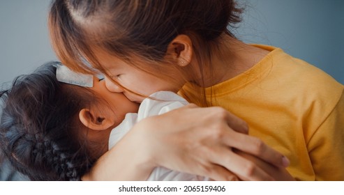 Happy Cheerful Asia Family Mom Holding Sick Toddler Girl In Arms And Attach Antipyretic Gel And Kiss On Baby Forehead In Living Room At House. Medical Care Insurance, Treatment And Healthcare Concept.