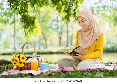 Happy cheerful Asian beautiful muslim woman sitting on the ground at the park and drinking a cup of tea in afternoon. Beautiful muslim woman relaxing and picnic in weekend. - Powered by Shutterstock