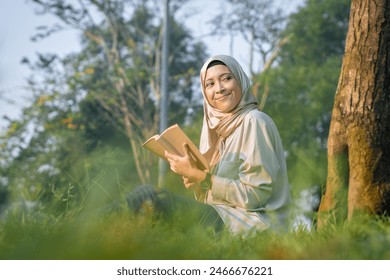 Happy cheerful Asian beautiful Muslim woman reading a book outdoor - Powered by Shutterstock