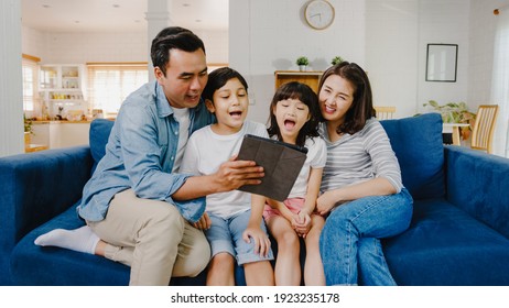 Happy cheerful Asian family dad, mom and kids having fun and using digital tablet video call on sofa at house. Self-isolation, stay at home, social distancing, quarantine for coronavirus prevention. - Powered by Shutterstock