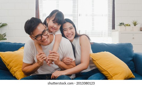 Happy Cheerful Asian Family Dad, Mom And Daughter Having Fun Cuddling And Video Call On Laptop On Sofa At House. Self-isolation, Stay At Home, Social Distancing, Quarantine For Coronavirus Prevention.