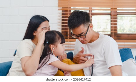 Happy Cheerful Asian Family Dad, Mom And Daughter Playing Funny Game As Doctor Having Fun On Sofa At Home. Self-isolation, Stay At Home, Social Distancing, Quarantine For Coronavirus Prevention.