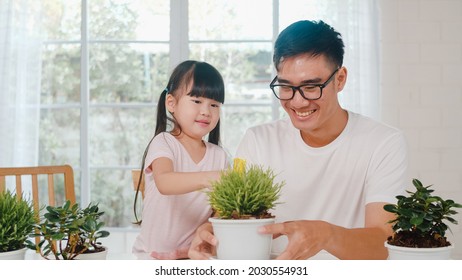 Happy Cheerful Asian Family Dad And Daughter Watering Plant In Gardening Near Window At House. Self-isolation, Stay At Home, Social Distancing, Quarantine For Coronavirus Prevention.