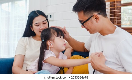 Happy Cheerful Asian Family Dad, Mom And Daughter Playing Funny Game As Doctor Having Fun On Sofa At Home. Self-isolation, Stay At Home, Social Distancing, Quarantine For Coronavirus Prevention.