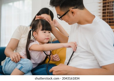 Happy Cheerful Asian Family Dad, Mom And Daughter Playing Funny Game As Doctor Having Fun On Sofa At Home. Self-isolation, Stay At Home, Social Distancing, Quarantine For Coronavirus Prevention.